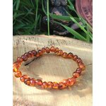 Bracelet ambre naturel posé sur support clair avec feuillage vert en fond, sérénité douce, réassurance et lumière intérieure