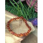 Bracelet ambre naturel couleur cognac sur fond clair avec plantes en arrière-plan, bien-être, vitalité douce et apaisement du mental