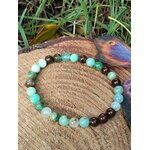 Bracelet chrysoprase vert pomme et perles marron sur rondin de bois avec herbe et feuille brune, réconfort émotionnel et douceur du cœur