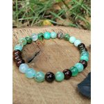 Bracelet chrysoprase sur tranche de bois avec verdure floue en arrière-plan, perles marron chocolat pour confiance calme et présence rassurée