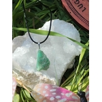 Pendentif chrysoprase verte sur cordon noir posé sur amas de quartz blanc avec feuilles vertes, pierre naturelle associée au calme intérieur, au renouveau et à la douceur du cœur.