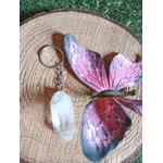 Porte-clés / bijou de sac en cristal de roche taillé en pointe facettée, avec anneau métal, posé sur une tranche de bois avec un papillon décoratif violet et rose, ambiance nature