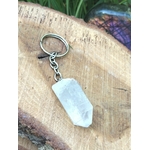 Porte-clés / bijou de sac en cristal de roche taillé en pointe facettée, avec chaîne et anneau métal, posé sur une tranche de bois clair en décor naturel