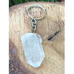 Porte-clés / bijou de sac en cristal de roche taillé en pointe facettée, avec anneau métallique, posé sur une tranche de bois clair en décor naturel