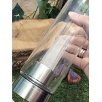 bouteille deau en verre énergisant cristal de roche, tenue en main, base inox, pointe de cristal de roche intégrée, photo sur décor nature bois