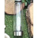 bouteille deau en verre énergisant cristal de roche, gros plan sur la pointe de cristal de roche intégrée, base inox, décor mousse verte et rondins de bois