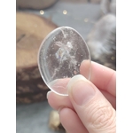 Galet cristal de roche poli tenu en main en gros plan, pierre roulée translucide avec inclusions naturelles associée à la simplicité, à la clarté et à l’équilibre intérieur.