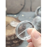 galet cristal de roche poli tenu entre les doigts, pierre roulée transparente avec inclusions naturelles, photo en gros plan