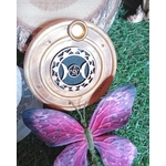 Porte-encens rond en bois motif Triple Lune, posé sur de l’herbe verte avec une décoration papillon violet au premier plan.