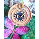 Porte-encens rond en bois motif Triple Lune, posé sur de la mousse verte avec un papillon violet en décor au premier plan