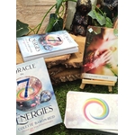 L’Oracle des 7 Énergies – coffret divinatoire en français avec boîte, cartes et dos au cercle multicolore, mise en scène sur mousse/bois avec feuillage et petit chevalet en bois.