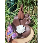 Porte-encens backflow Mains Lotus en terre cuite brun foncé, posé sur rondin de bois en extérieur, décor herbe verte avec papillon violet en avant-plan