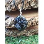 Pendentif indigo gabbro poli suspendu devant rondins en ambiance nature, pierre naturelle associée à la stabilité émotionnelle, à l’aplomb et au recentrage.