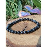 Bracelet Indigo Gabbro perles polies sur rondin, feuillage vert en arrière-plan, pierre naturelle liée à l’équilibre émotionnel