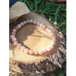 Bracelet pierre de soleil 6 mm orange pêche lumineux en perles rondes posé sur un rondin de bois, avec herbes vertes en fond, évoquant la joie, la chaleur intérieure et l’optimisme