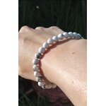 Bracelet howlite blanche 6 mm porté au poignet sur fond sombre, perles blanches veinées de gris pour calme du cœur, retenue émotionnelle et sérénité