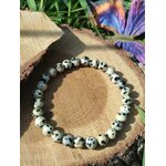 Bracelet jaspe dalmatien 6 mm sur bois avec fleur violette en arrière-plan, perles ivoire mouchetées de noir pour discernement et calme protecteur