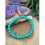 bracelet turquoise stabilisée perles rondes posé sur rondin de bois avec papillon violet protection en voyage et bouclier énergétique