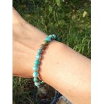 Bracelet turquoise du Tibet porté au poignet avec fond feuillage, pierre naturelle liée au calme mental et à l’expression apaisée