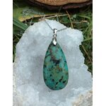 Pendentif turquoise africaine forme goutte sur bélière argentée, suspendu sur amas de quartz brut avec décor herbe et bois, jaspe africain associé au recentrage, à l’expression calme et à l’équilibre intérieur.