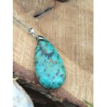 Pendentif turquoise africaine goutte bleu-vert sur bélière argentée, posé sur bois clair, jaspe africain lié à la présence à soi, à la souplesse émotionnelle et à la communication calme.
