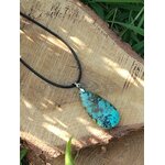 Collier cordon noir avec pendentif turquoise africaine goutte bleu-vert marbrée posé sur rondelle de bois avec herbe, jaspe africain évoquant l’ancrage, la clarté intérieure et l’expression posée.