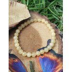 Bracelet calcite jaune sur rondin de bois avec feuillage vert et papillon, pierre naturelle liée à la concentration et au moral