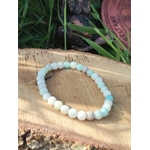 Bracelet amazonite multicolore en perles 6 mm, posé sur rondin de bois avec feuillage vert et détail naturel en fond ; pierre associée à l’apaisement, à la confiance et à l’équilibre émotionnel.
