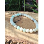 Bracelet amazonite multicolore en perles 6 mm, posé sur rondin de bois avec feuillage vert en arrière-plan ; pierre associée à l’apaisement, à l’équilibre émotionnel et à une communication plus douce.