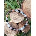 Bracelet Deuil mis en scène sur rondins de bois avec feuillage vert, aide à traverser les vagues émotionnelles et à retrouver un appui plus stable