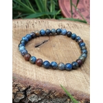 Bracelet dumortiérite en perles bleu denim et bleu profond sur support bois avec feuillage vert, discipline intérieure, focus et expression sereine