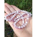 Fil de perles kunzite 6 mm tenu en main devant feuillage, tons rose pastel et lilas clair pour délicatesse intérieure, appui émotionnel et douceur stable