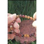 Bracelet mookaïte 6 mm porté au poignet, perles ocre, beige, bordeaux et prune, avec plaque en cuivre triquetra et feuillage vert, assurance, centrage et équilibre intérieur