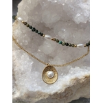 Collier double chaîne dorée en acier inoxydable avec perles blanches, pierres vertes et médaillon nacré, présenté sur buste blanc, gros plan sur le pendentif, fond clair et amas de quartz en décor.