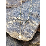 Collier double chaîne dorée en acier inoxydable avec perles blanches, pierres vertes et médaillon nacré, suspendu sur une pierre gris bleuté texturée, décor naturel, lumière douce.