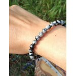 Bracelet obsidienne neige 6 mm porté au poignet, perles noir profond et gris moucheté, photo en extérieur avec feuillage, stabilité, protection, clarté mentale, recentrage.