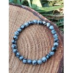 Bracelet obsidienne neige 6 mm porté au poignet, perles noir profond et gris moucheté, photo en extérieur avec feuillage, stabilité, protection, clarté mentale, recentrage.
