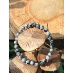 Bracelet obsidienne neige 6 mm posé sur galet clair avec feuillage en arrière-plan, perles noir profond et gris nuage pour clarté du mental et stabilité émotionnelle