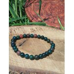 Bracelet jaspe héliotrope 6 mm sur rondin de bois, verdure en fond ; stabilité, apaisement, confiance.