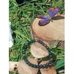 Bracelet jaspe héliotrope 6 mm sur rondin de bois, papillon violet et herbes autour ; énergie, détermination, recentrage.