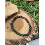 Bracelet jaspe héliotrope 6 mm sur rondin de bois, herbes en fond, lumière naturelle ; ancrage, calme, courage.