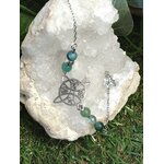 Bracelet symbole antique noir, amazonite et apatite bleu-vert avec Aqua Aura, présenté sur quartz brut et mousse, calme, communication, lucidité, stabilité émotionnelle.