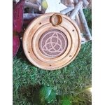 Porte-encens bois rond triquetra, posé sur mousse verte avec décor branches en bois et touche bordeaux en arrière-plan, ambiance nature.