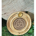 Porte-encens rond en bois motif triquetra, posé sur planche claire avec verdure en fond, ambiance protection, harmonie, rituel.