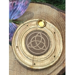 Porte-encens bois rond triquetra, posé sur tranche de bois brut avec papillon bleu-violet en décor, fond végétal sombre, ambiance calme.