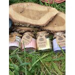 Bougies cire de soja en petits pots verre, couvercles liège, posées dans l’herbe au pied d’une tranche de bois, harmonie, détente, réconfort.
