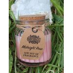 Bougie parfumée Rose de Minuit en cire de soja, pot en verre avec couvercle en liège et étiquette kraft, posée dans l’herbe en décor naturel, ambiance douce, détente, apaisement, cocooning.