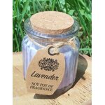 Bougie lavande en pot de verre violet strié avec couvercle en liège et étiquette kraft, photo en extérieur sur support bois, herbe en arrière-plan, ambiance calme et apaisante.