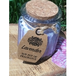 Bougie parfumée lavande en pot de verre strié violet avec couvercle en liège, ficelle et étiquette kraft, posée sur planche en bois avec herbe en arrière-plan et papillon violet à côté, ambiance douce, apaisante, détente, sérénité.