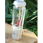 Spell jar en fiole de verre avec cristal de roche, fil rouge, cire blanche et breloque triquetra, posé sur bois en extérieur, ambiance protection et clarté.